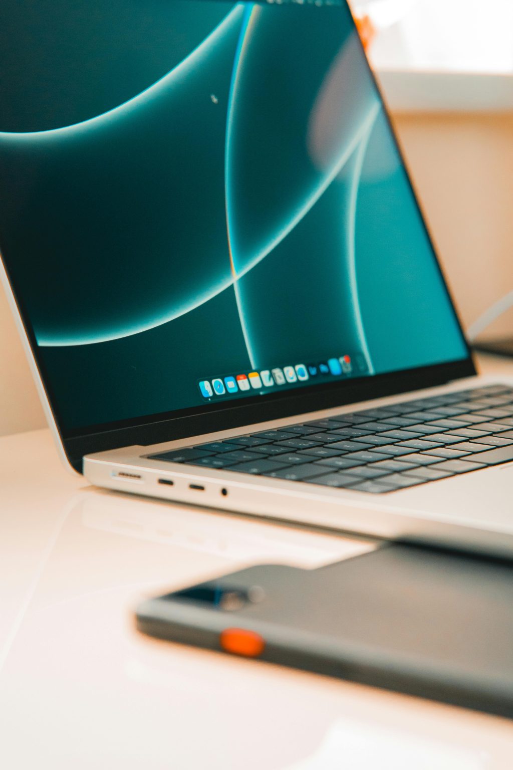 used macbooks A close-up of a sleek laptop and smartphone on a desk, showcasing modern technology.