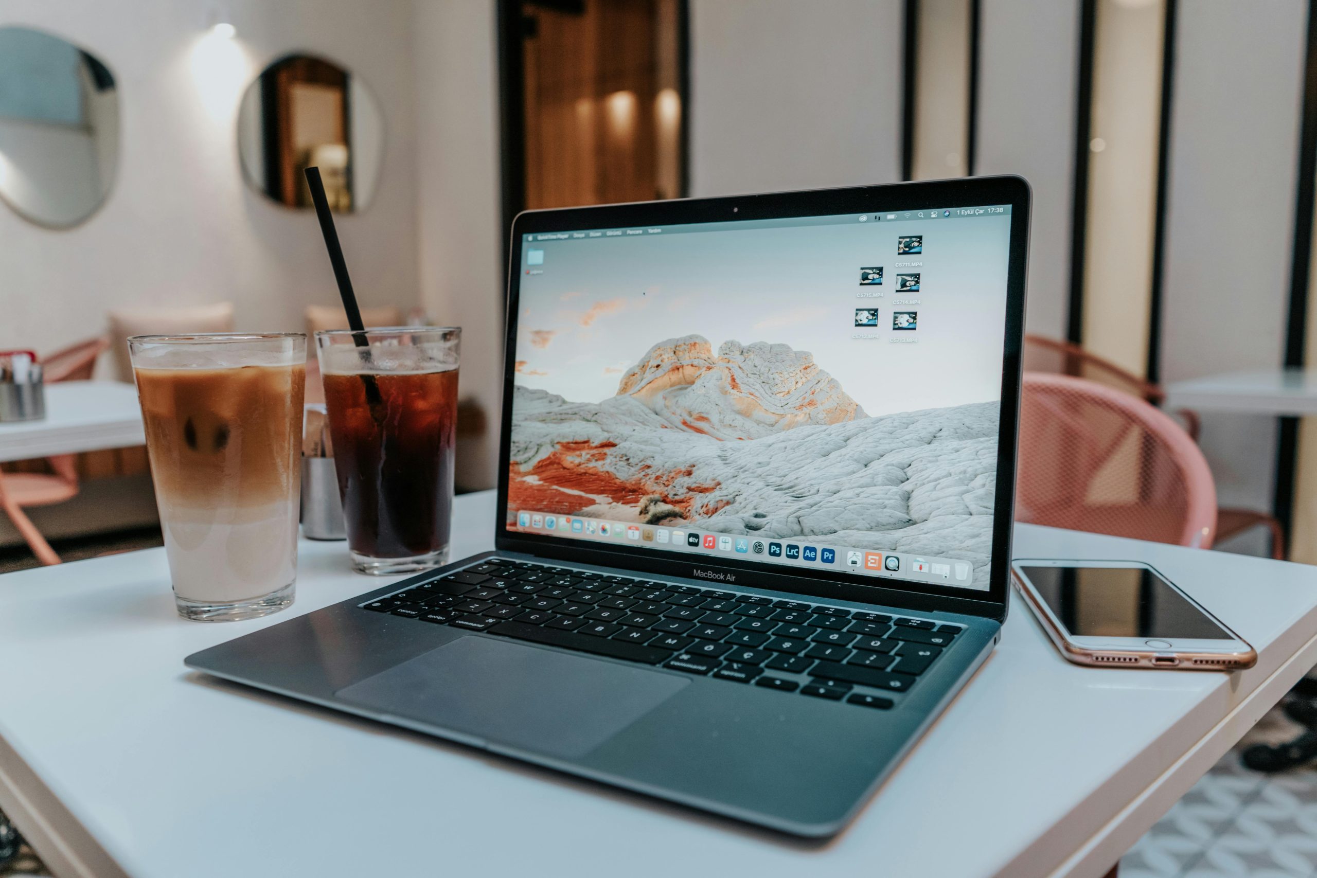 A stylish workspace featuring a MacBook Air, iced coffee, and smartphone on a white table indoors.